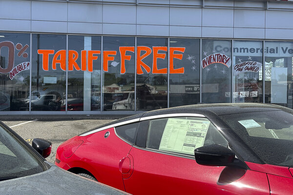 A "Tariff Free" sign, written in bright orange letters on glass showroom windows, appears at a New Jersey car dealership.